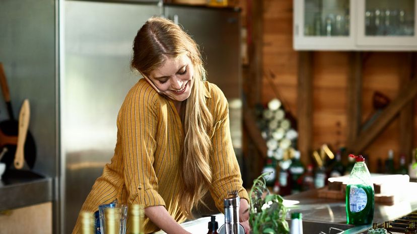 Attractive woman using phone and doing dishes