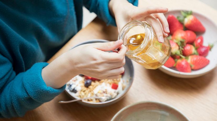 Woman takes honey from jar with spoon for breakfast