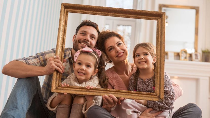 Smiling family having fun with a picture frame at home