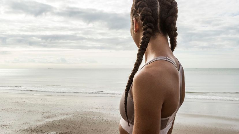 Young female runner with hair plaits looking out to sea from beach