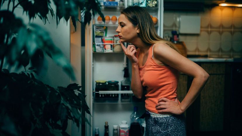 Young woman looking for midnight snack in the refrigerator at home