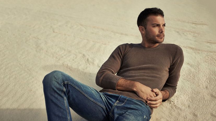 handsome man laying back brown shirt jeans on sand scruffy
