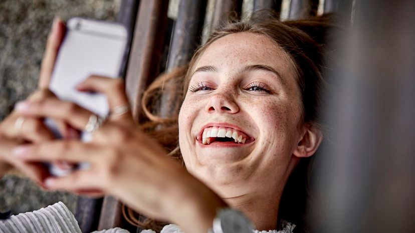 Laughing young woman lying on a bench using cell phone