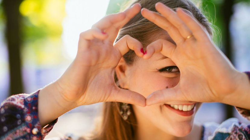 Smiling girl looking through a hand heart