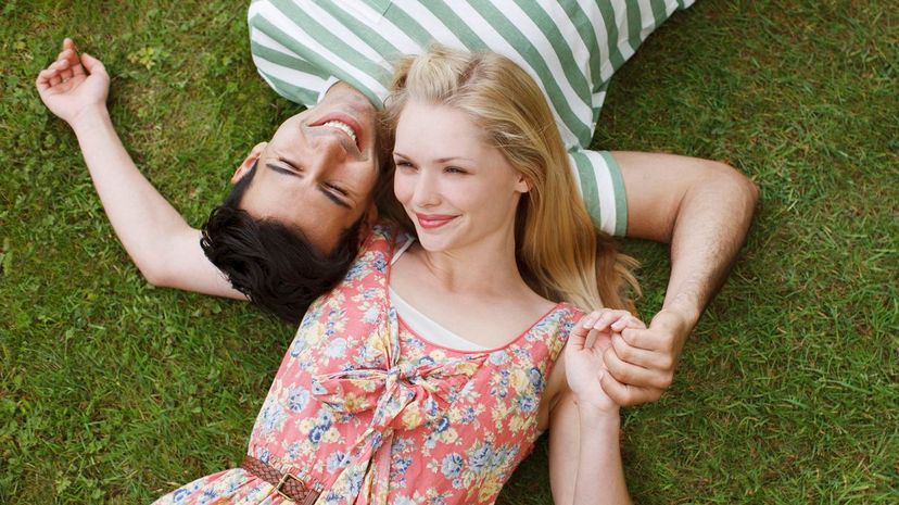 Young couple laying on grass and holding hands