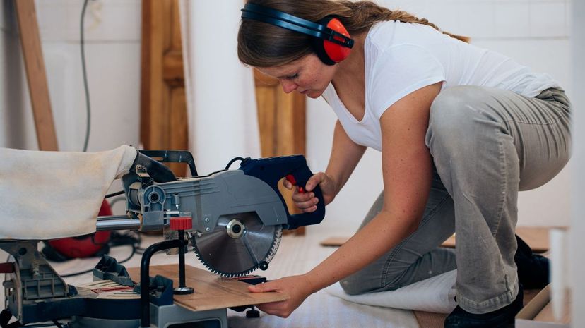 Woman installing laminate flooring, using a saw indoor