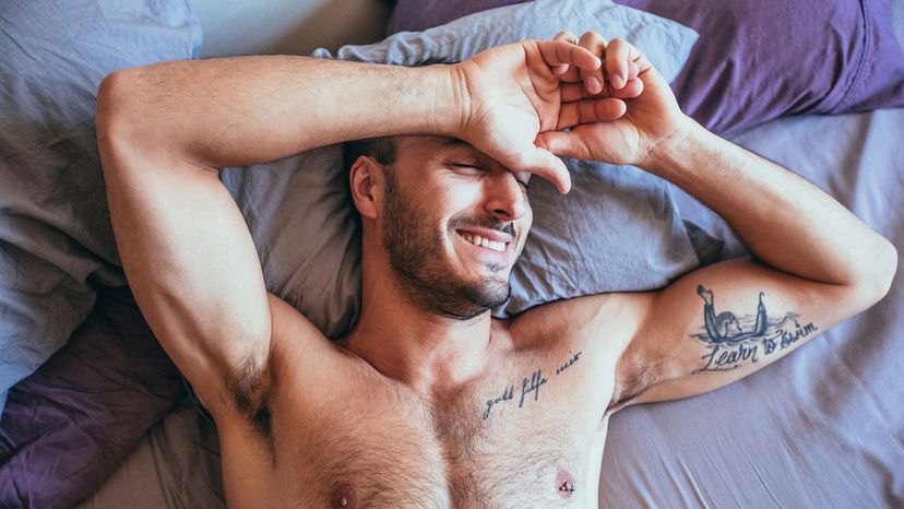 handsome man in bed purple sheets tattoos smiling shirtless