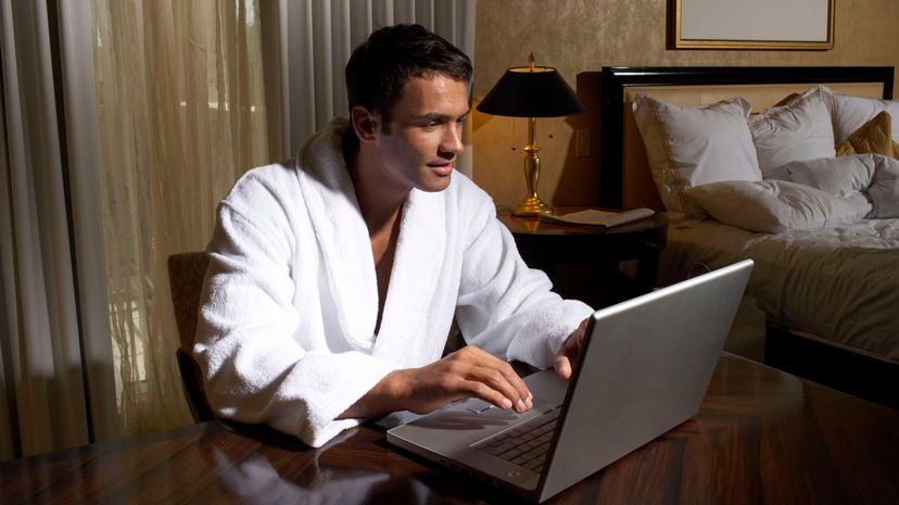 Man wearing bathrobe using laptop in bedroom