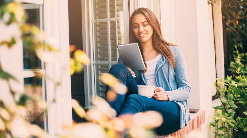 Woman holding a cup of and tablet outside window