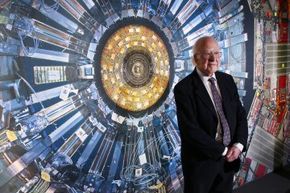 彼得·希格斯教授站在科学博物馆“对撞机”的大型强子对撞机的照片前。展览于2013年11月12日在英国伦敦举行。＂width=
