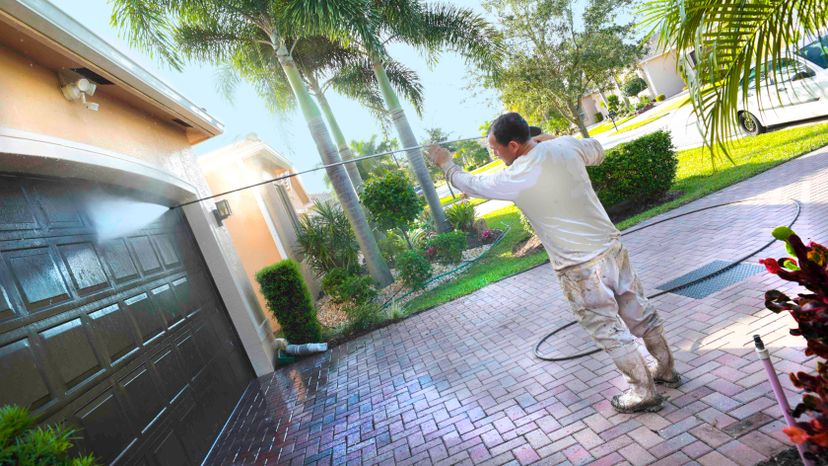 A man pressure washing a brown garage door.