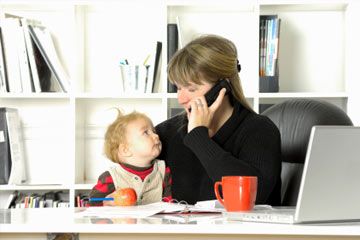 A working mother with a baby on her lap while working at her desk.