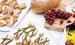 An appetizer spread including small bites on toast, bread, cheese, grapes and a salad