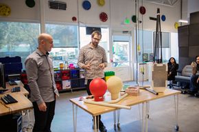 Two members of the Google X team show off the round antannea and blocky parcel for Google Loon, an experimental, balloon-based Internet provider.