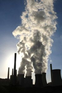 Silhouette of power plant with smoke stacks and pollution billowing out.