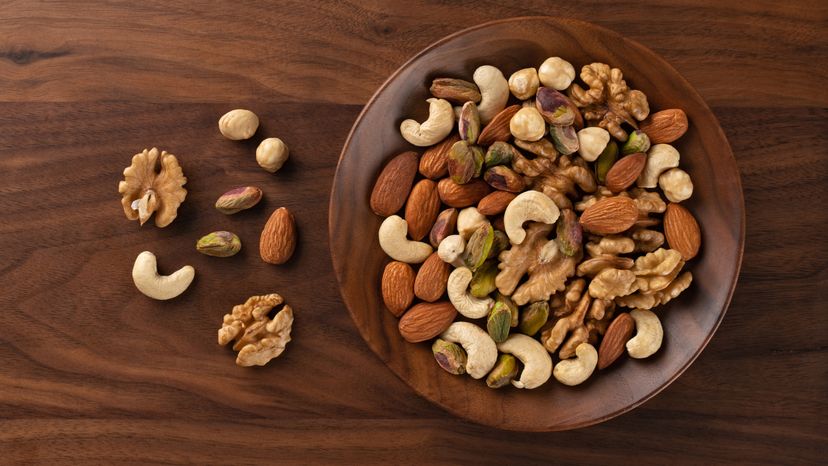 Assorted Nuts of Almond,Cashew,Hazelnut,Pistachio and Walnut Mixed in a Wood Bowl on Brown Wood Table Directly Above View.