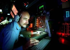 A man wearing a headset sits surrounded by radar equipment that he is operating.