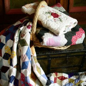 A collection of hand-made quilts lie atop an antique trunk.