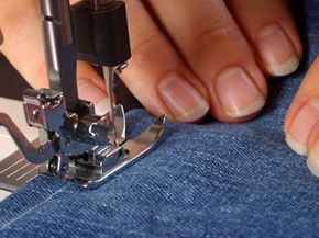 Closeup detail of hands stitching blue denim fabric with a sewing machine.