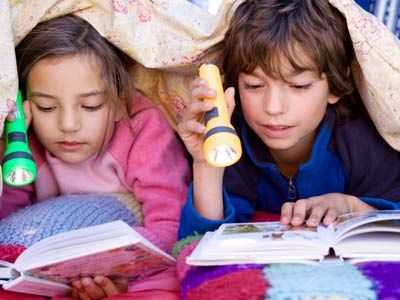boy and girl read by flashlight under the covers
