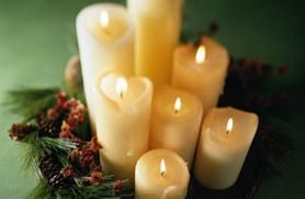 A group of seven lit soy candles surrounded by a greenery wreath with pinecones.