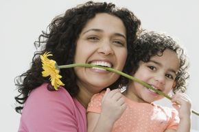 A woman with her daughter holding a flower in their teeth.
