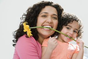 A woman with her daughter holding a flower in their teeth.