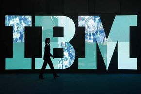 在德国汉诺威举行的2011年CeBIT技术贸易博览会上，一名妇女走过IBM的标志。商学院经常研究IBM的革新。”border=