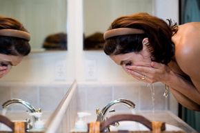 Woman removes makeup at bathroom sink.