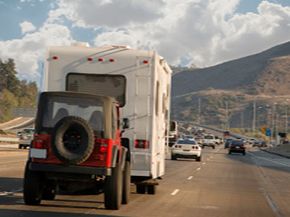 A trailer drives along a highway with a small jeep in tow.