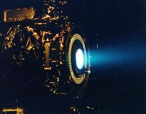 This image of a xenon ion engine, photographed through a port of the vacuum chamber where it was being tested at NASA's Jet Propulsion Laboratory, shows the faint blue glow of charged atoms being emitted from the engine. The ion propulsion engine is the first non-chemical propulsion to be used as the primary means of propelling a spacecraft.