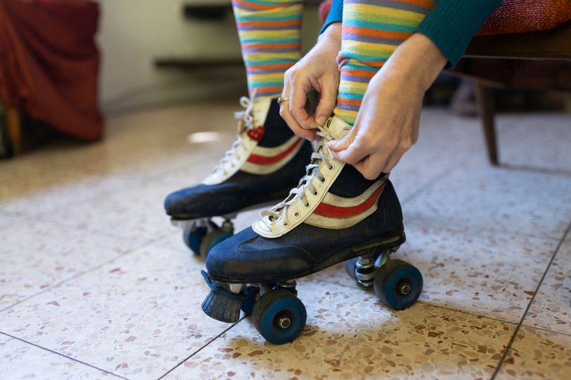 Close-up of womans hands tying the shoe laces of vintage roller skates over colourful striped socks.