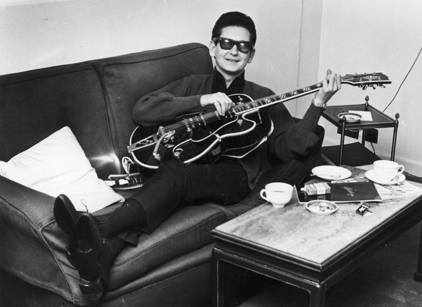 singer roy orbison reclines on a couch holding a guitar