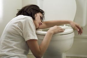 A sick woman leans on a toilet bowl.