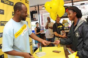Musician Wyclef Jean (l) passes out $50 Western Union gift cards to fans at an event in Los Angeles. Western Union earnings help to measure migration trends.