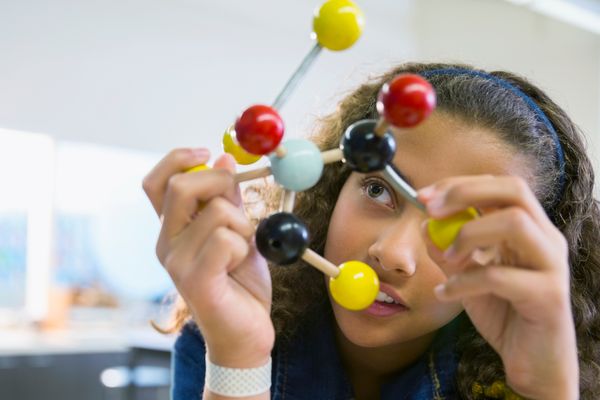 An elementary student holds a molecular model in her hand and looks at it.