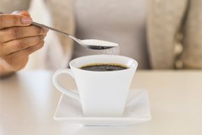 Sugar cascades from a spoon held above a cup of black coffee.