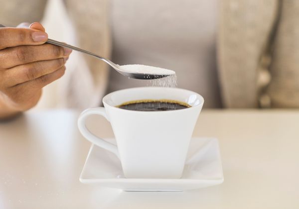 Sugar cascades from a spoon held above a cup of black coffee.