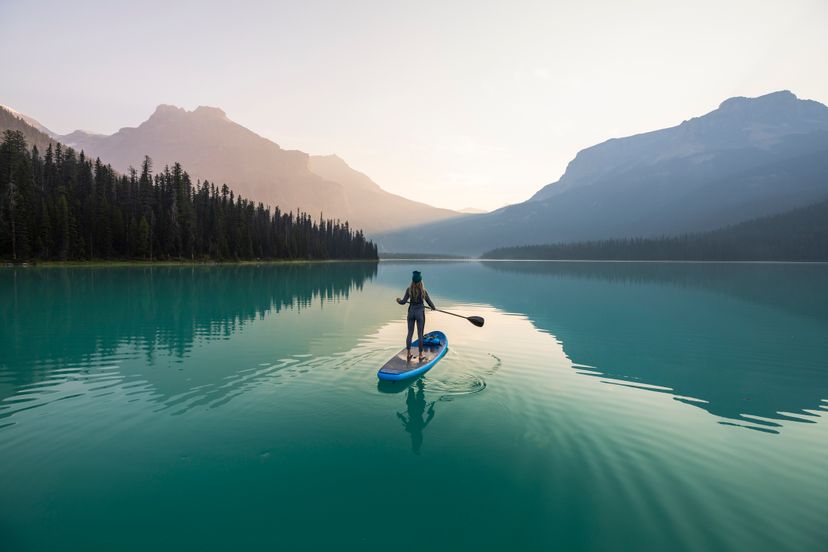 A young woman paddleboarding on Emerald Lake at sunrise in Yoho National Park.