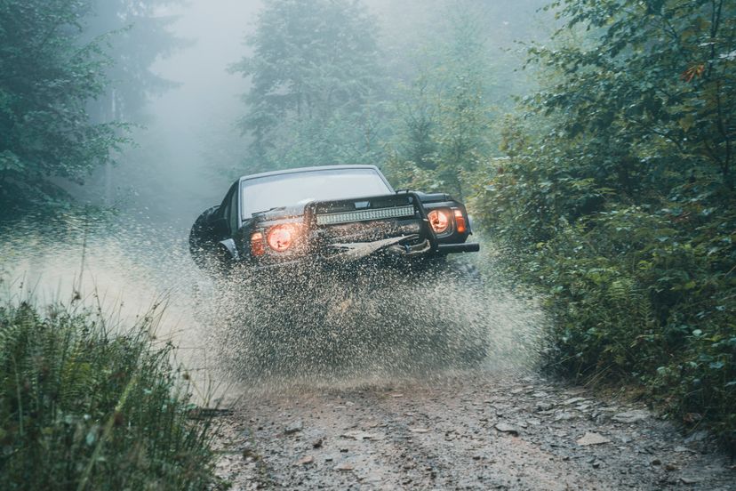 Customized off-road vehicle with big wheels is driving on a wet road in the forest.