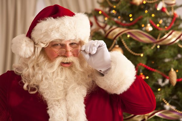 Santa Claus peering over glasses in front of Christmas tree