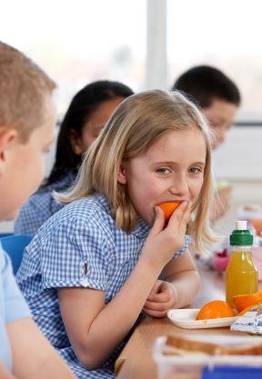 Young girl eating an orange at a school lunch table
