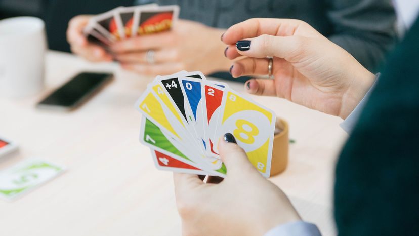 A person with black nail polish holding Uno cards at a table with others playing the game