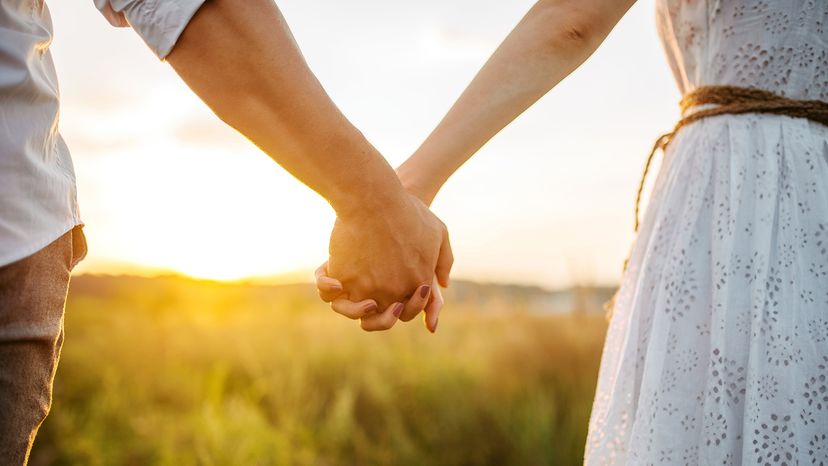 Couple hold hands in green field on sunset
