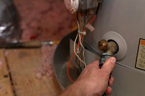 Hand attaches hose to a water heater drain to perform maintenance.