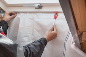 Close up of a person installing vapor barrier around the skylight in the attic of a house.