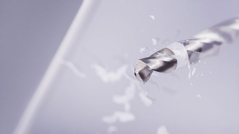 A drill bit drilling through a piece of glass.