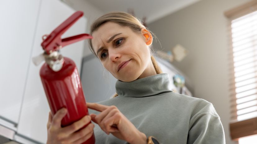 A woman looks at the fire extinguisher expiration date at home.