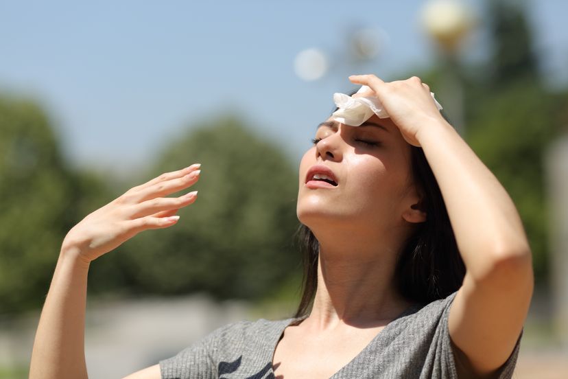 A woman sweats and fans herself with her hand in direct sunlight