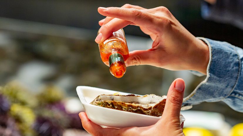 Person pours Tabasco on an oyster at the Paris Market in Bastille